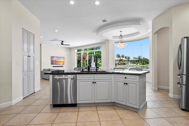 kitchen featuring light tile patterned floors, ceiling fan with notable chandelier, a tray ceiling, appliances with stainless steel finishes, and sink