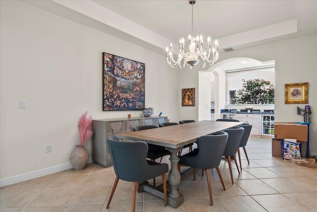 dining space with a tray ceiling, a notable chandelier, and light tile patterned floors