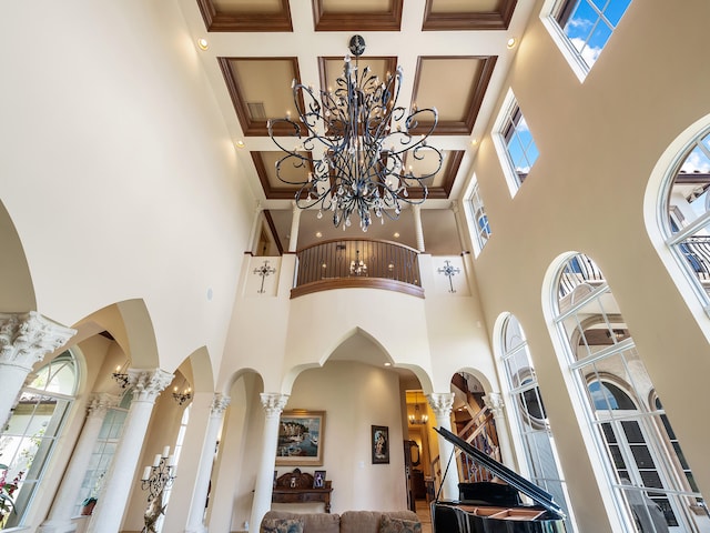 interior space with a towering ceiling, a notable chandelier, coffered ceiling, and decorative columns