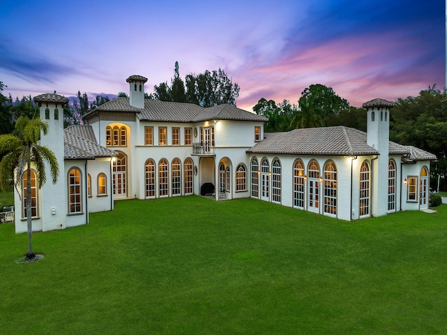 back house at dusk with french doors and a lawn