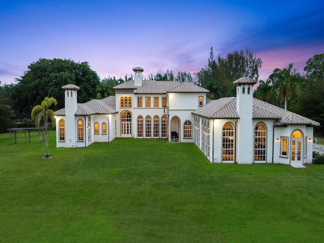 back house at dusk with french doors and a lawn