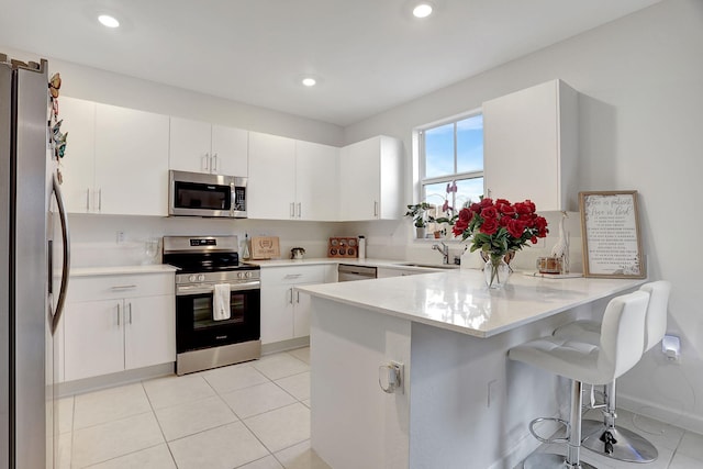 kitchen with a kitchen breakfast bar, kitchen peninsula, sink, appliances with stainless steel finishes, and white cabinets