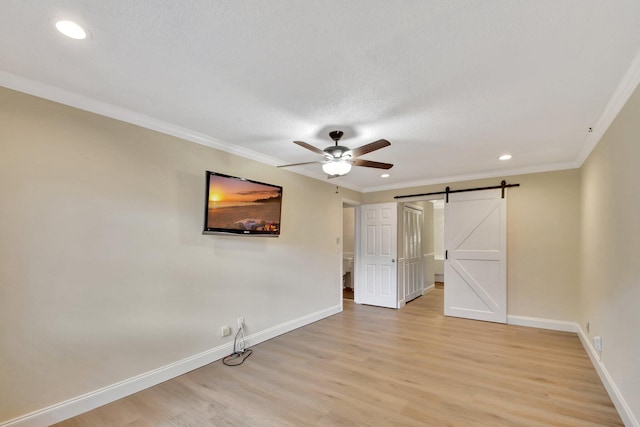 unfurnished bedroom featuring ceiling fan, a barn door, crown molding, and light hardwood / wood-style flooring