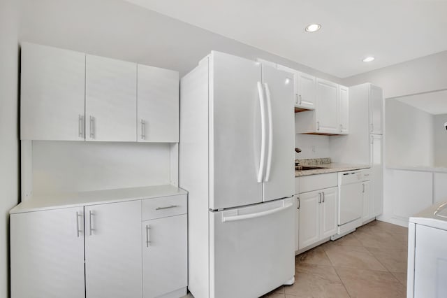 kitchen featuring white appliances, sink, washer / dryer, light tile patterned flooring, and white cabinetry