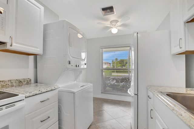 clothes washing area featuring stacked washer / dryer, light tile patterned floors, and ceiling fan