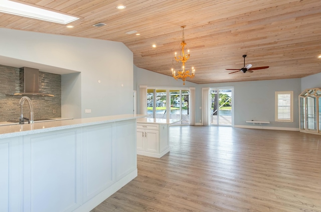 interior space featuring wall chimney range hood, light stone countertops, decorative light fixtures, white cabinetry, and wood ceiling