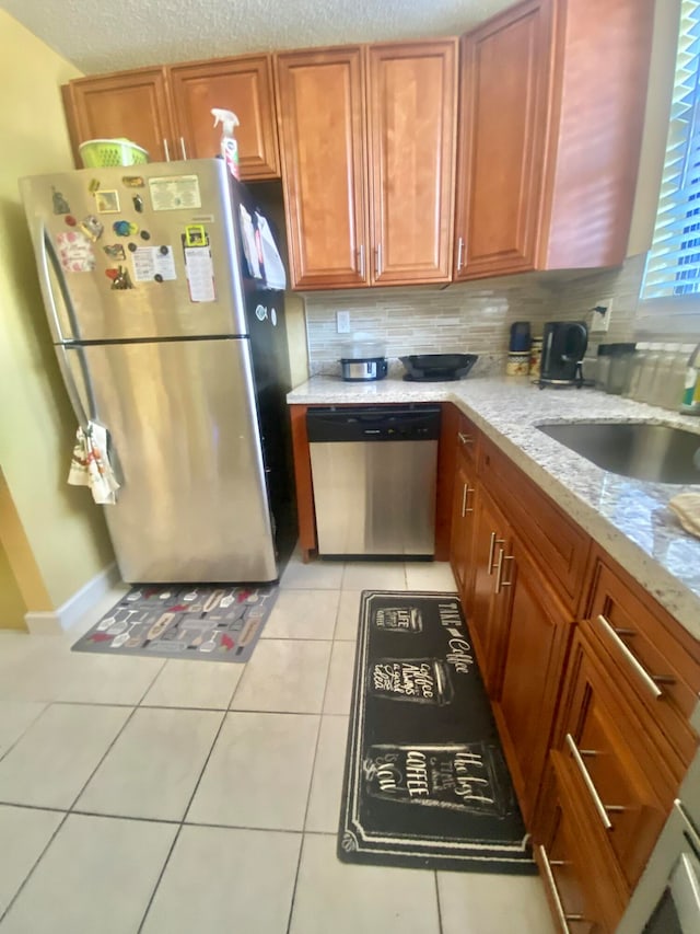 kitchen with light stone counters, light tile flooring, stainless steel appliances, backsplash, and sink