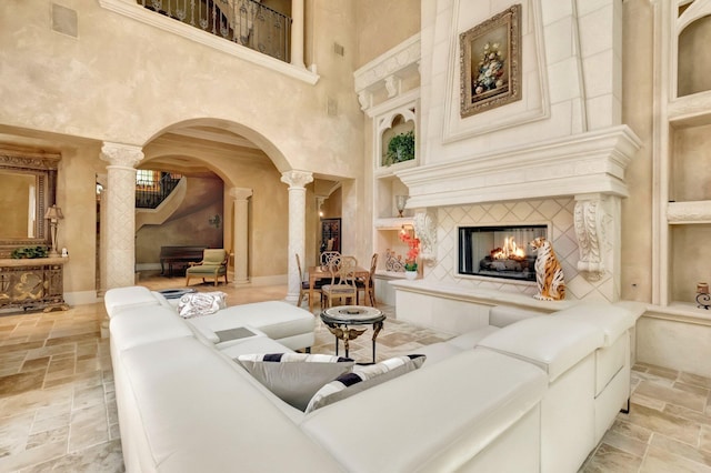 living room featuring built in shelves, a tiled fireplace, a high ceiling, and decorative columns