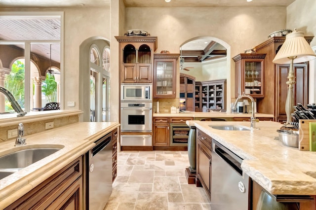 kitchen with beam ceiling, sink, coffered ceiling, light stone counters, and appliances with stainless steel finishes