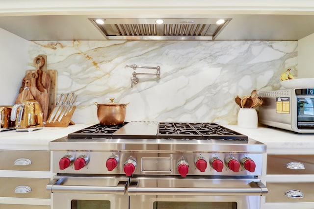 kitchen with decorative backsplash, range hood, and range with two ovens