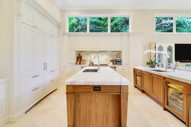 kitchen with decorative backsplash, a center island with sink, white cabinets, and sink