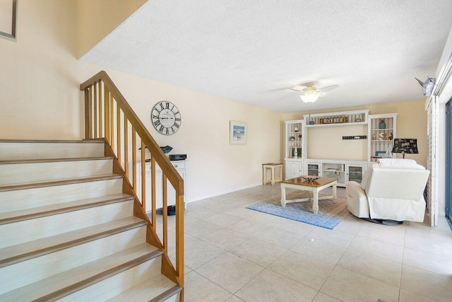 living room with a textured ceiling, ceiling fan, stairway, and light tile patterned flooring