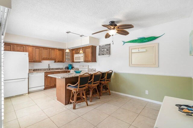 kitchen featuring white appliances, a kitchen breakfast bar, hanging light fixtures, ceiling fan, and kitchen peninsula