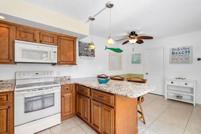 kitchen featuring a breakfast bar, white appliances, decorative light fixtures, light tile patterned flooring, and kitchen peninsula