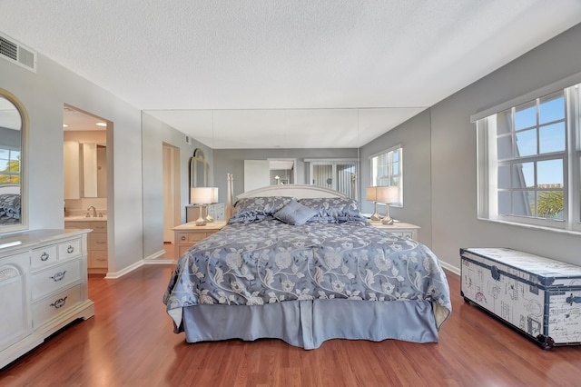 bedroom featuring connected bathroom, dark hardwood / wood-style floors, and a textured ceiling