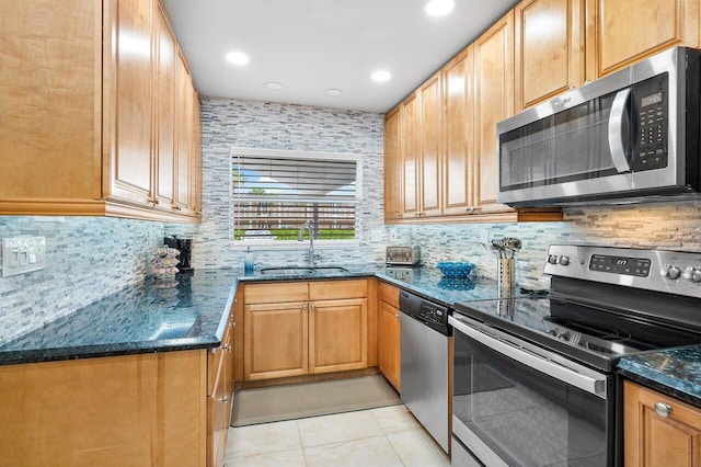 kitchen with sink, tasteful backsplash, dark stone countertops, light tile patterned floors, and appliances with stainless steel finishes