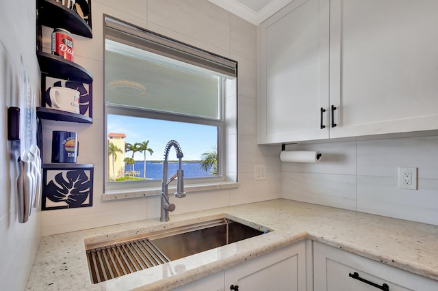 kitchen with light stone counters, white cabinets, ornamental molding, sink, and a water view