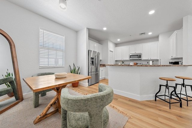 kitchen with light wood-type flooring, appliances with stainless steel finishes, white cabinets, kitchen peninsula, and stone counters