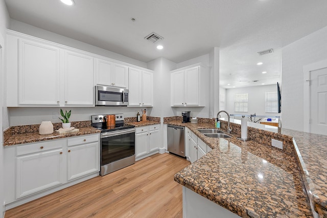 kitchen with white cabinets, dark stone counters, light hardwood / wood-style floors, stainless steel appliances, and sink