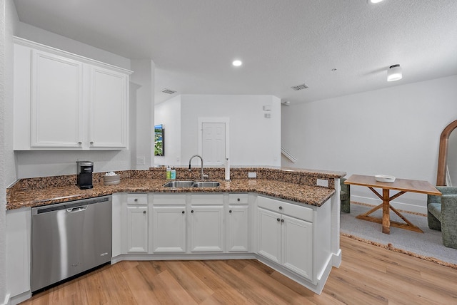 kitchen featuring kitchen peninsula, white cabinetry, stainless steel dishwasher, light wood-type flooring, and dark stone countertops