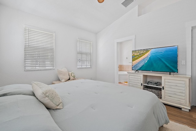 bedroom with ceiling fan, connected bathroom, vaulted ceiling, and hardwood / wood-style floors