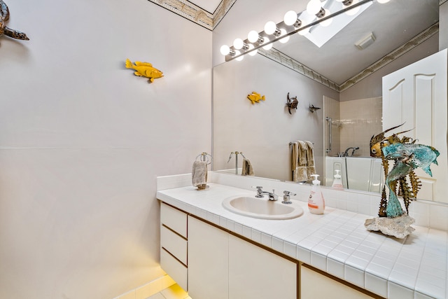 bathroom with a tile shower, ornamental molding, lofted ceiling with skylight, and oversized vanity