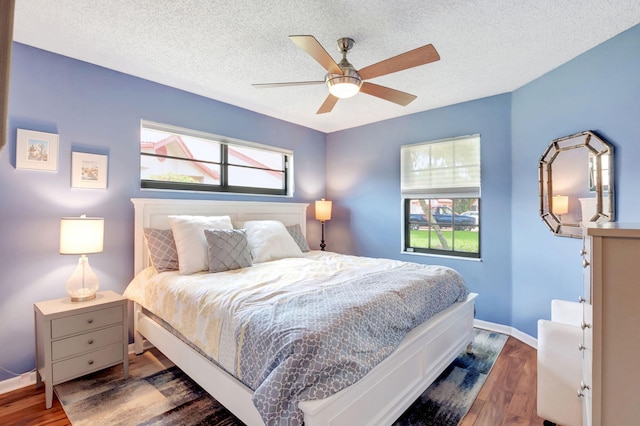 bedroom with ceiling fan, dark hardwood / wood-style flooring, a textured ceiling, and multiple windows