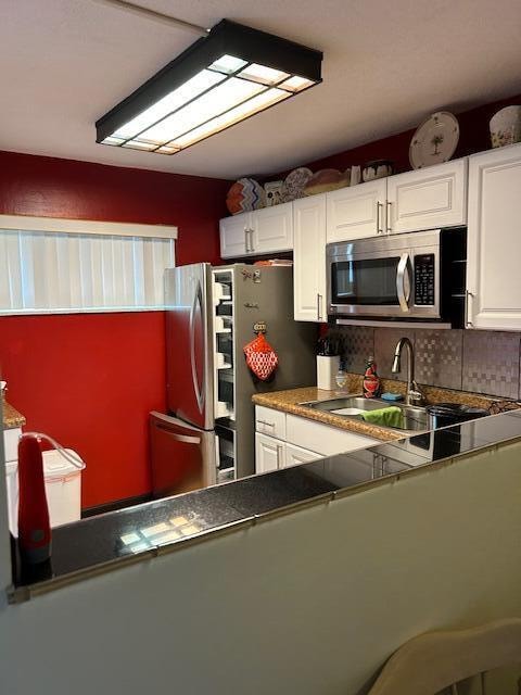 kitchen with appliances with stainless steel finishes, white cabinetry, sink, and backsplash