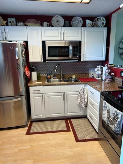 kitchen with stainless steel appliances, light hardwood / wood-style floors, white cabinets, and sink