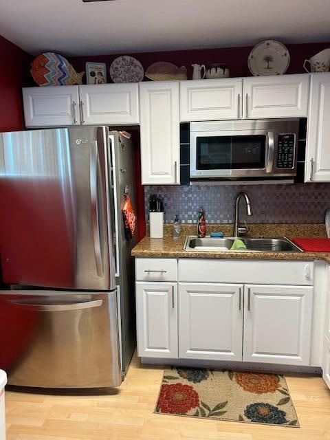 kitchen featuring light hardwood / wood-style flooring, appliances with stainless steel finishes, white cabinets, sink, and tasteful backsplash