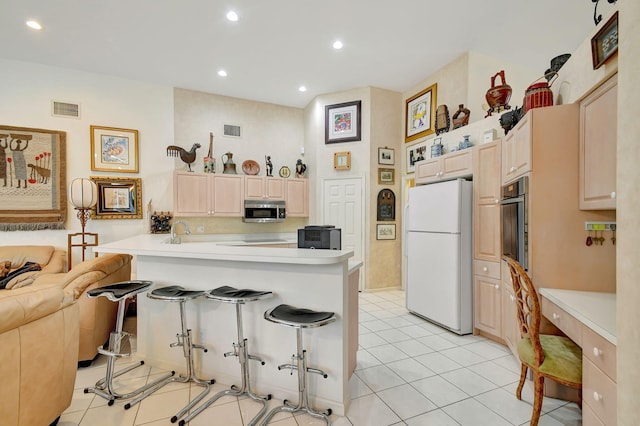 kitchen featuring kitchen peninsula, light tile patterned floors, appliances with stainless steel finishes, a kitchen breakfast bar, and sink