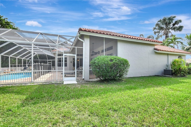 rear view of house featuring central air condition unit, a patio area, a lawn, and glass enclosure