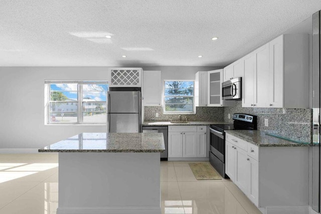 kitchen with stainless steel appliances, white cabinetry, dark stone countertops, and light tile patterned flooring