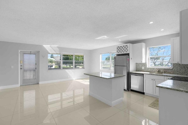 kitchen with white cabinetry, a kitchen island, stainless steel appliances, backsplash, and light tile flooring