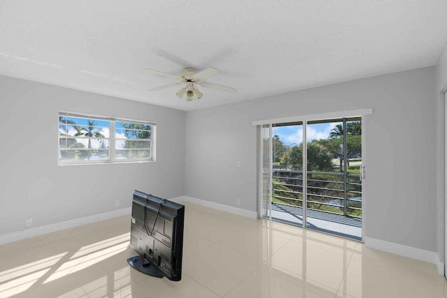 spare room with a healthy amount of sunlight, a wood stove, ceiling fan, and light tile floors