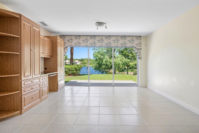 unfurnished room with light tile patterned flooring, a water view, and a textured ceiling