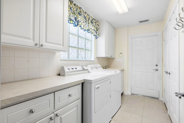 laundry area featuring washing machine and clothes dryer, light tile patterned flooring, and cabinets