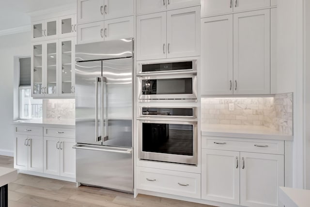 kitchen with stainless steel appliances, white cabinets, light countertops, backsplash, and glass insert cabinets