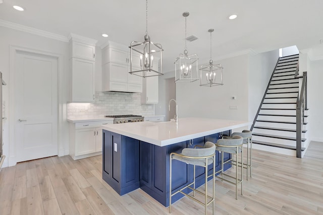 kitchen with pendant lighting, light countertops, visible vents, white cabinetry, and a large island with sink