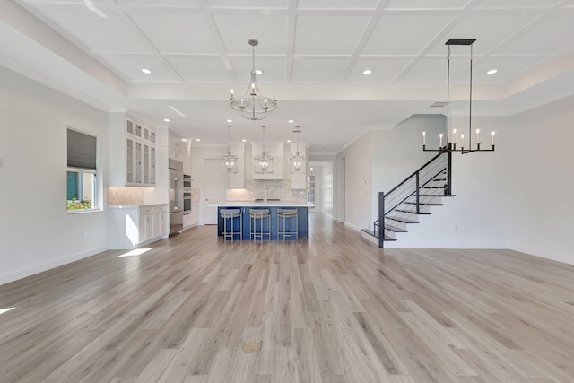 unfurnished living room featuring light wood finished floors, baseboards, coffered ceiling, stairway, and a sink