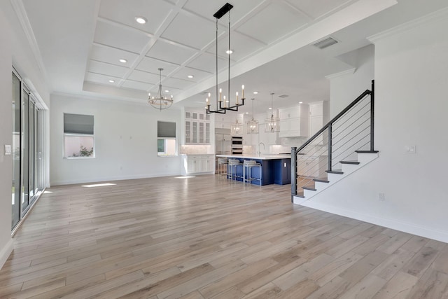 unfurnished living room featuring visible vents, light wood-style flooring, coffered ceiling, baseboards, and stairs