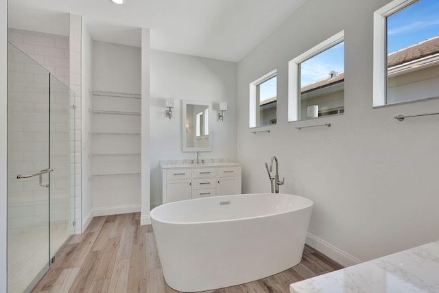 bathroom with a soaking tub, vanity, a shower stall, wood finished floors, and baseboards