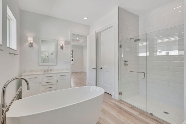 bathroom with recessed lighting, vanity, a shower stall, wood finished floors, and a freestanding tub