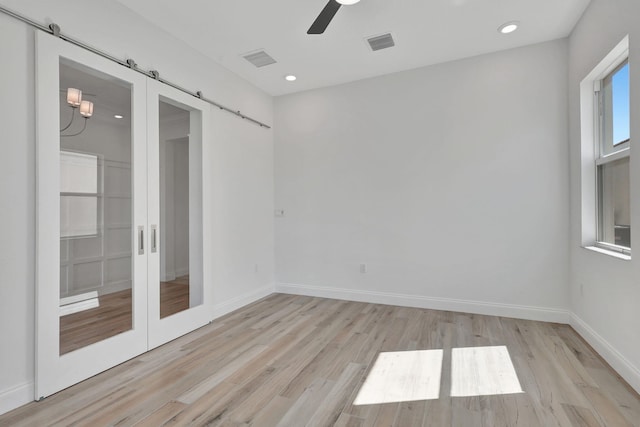 unfurnished room with light wood-type flooring, visible vents, baseboards, and a barn door