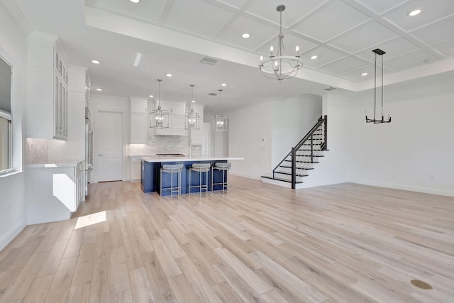 unfurnished living room with visible vents, coffered ceiling, stairs, light wood-type flooring, and a notable chandelier