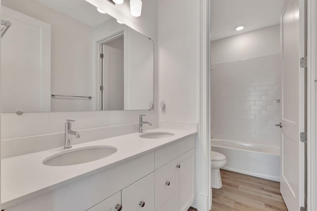 full bath with double vanity, a sink, toilet, and wood finished floors