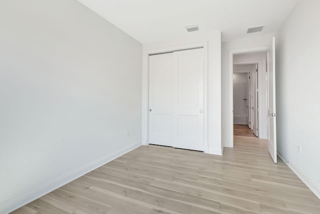 unfurnished bedroom featuring light wood finished floors, baseboards, visible vents, and a closet