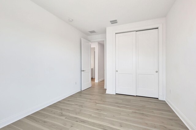 unfurnished bedroom featuring light wood finished floors, visible vents, baseboards, and a closet