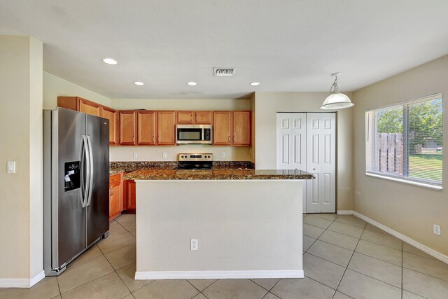 kitchen featuring stainless steel appliances, dark stone countertops, hanging light fixtures, light tile patterned flooring, and a center island