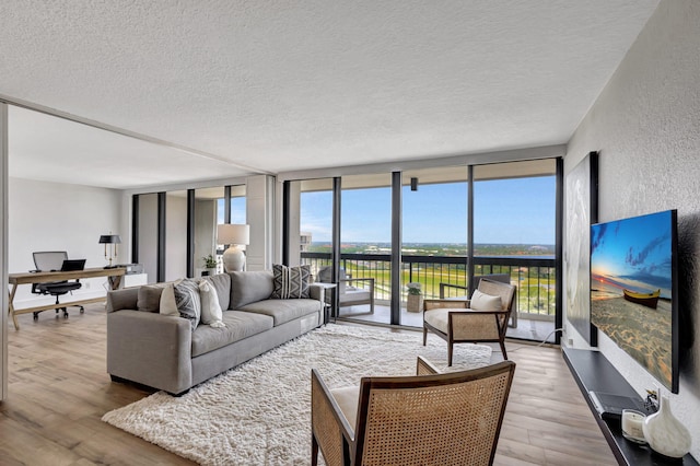 living room featuring wood-type flooring, a textured ceiling, and a wall of windows